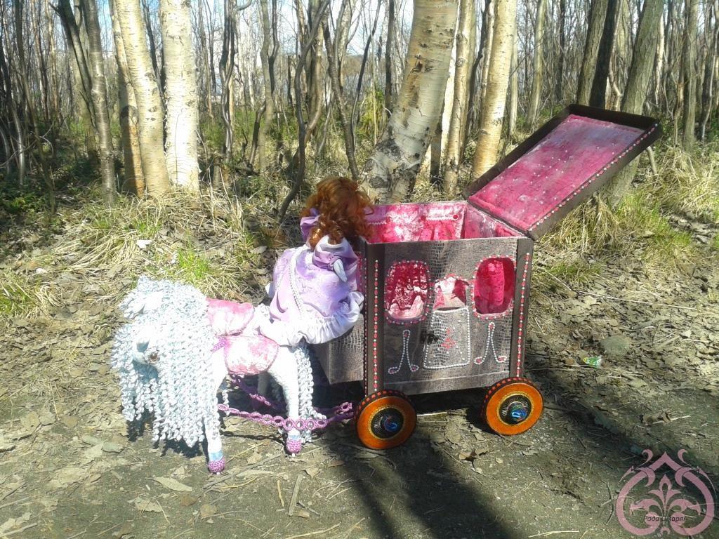 Кукла в карете едет по лесу.